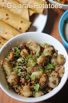 two bowls filled with food next to some pita bread on top of a wooden table