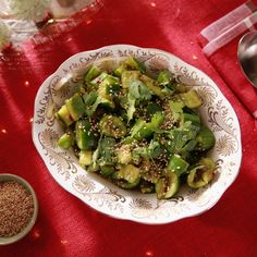 a white bowl filled with vegetables on top of a red table cloth next to a spoon