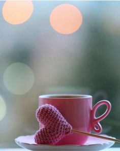 a pink knitted heart sitting on top of a white plate next to a cup