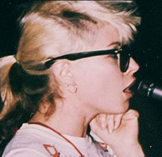 a woman with glasses on singing into a microphone