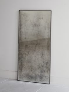 a large mirror sitting on top of a floor next to a white wall with a black frame