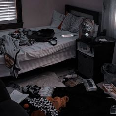 an unmade bed in a messy room with clothes on the floor and other items scattered around