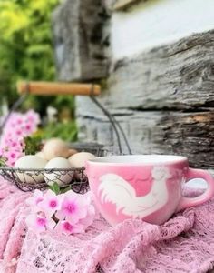 a pink coffee cup sitting on top of a table next to some flowers and eggs