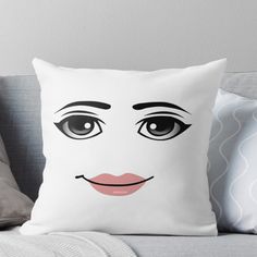 a white pillow with a black and pink face on the front, sitting on a couch