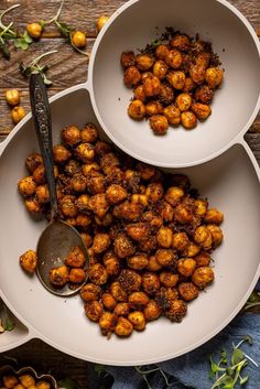 two white bowls filled with chickpeas next to a spoon on a wooden table