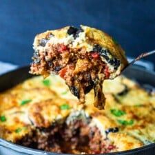 a close up of a spoonful of food in a casserole dish with meat and cheese