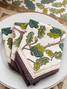 three napkins with green leaves on them sitting on a plate