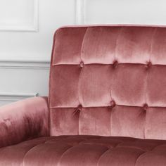 a pink velvet couch sitting on top of a wooden floor next to a white wall