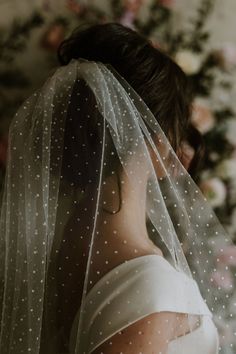 a woman wearing a wedding veil with polka dots on her head and shoulder, in front of flowers