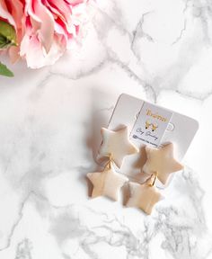 two star shaped earrings sitting on top of a marble table next to a pink flower