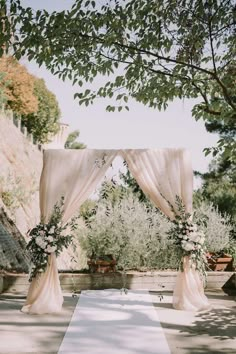 an outdoor ceremony setup with white drapes and greenery