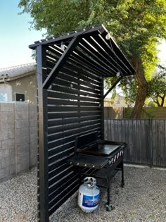 an outdoor bbq grill with a gas tank underneath it and a fence in the background