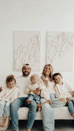 a family sitting on a couch in front of two paintings and one is holding their children