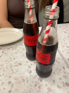 two coke bottles with straws in them sitting on a table