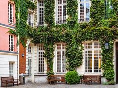 an old building covered in ivy with two benches next to it and several windows on the side