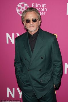 a man in a suit and sunglasses standing on a red carpet with a pink background