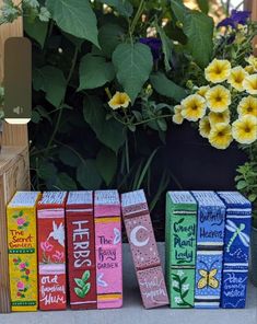 four colorful books are sitting on the ground next to some flowers and potted plants