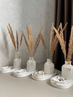 four white vases with dried plants in them