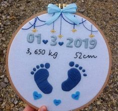 someone is holding up a cross stitch baby's birth date ornament with footprints on it