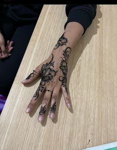 a woman's hand with henna tattoos sitting on top of a wooden table