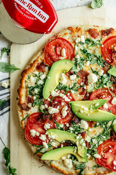 a pizza topped with tomatoes, avocado and feta cheese on a cutting board