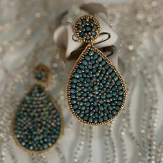 a pair of blue and gold earrings sitting on top of a white cloth covered table