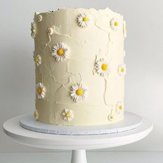 a white cake with yellow and white daisies on the top is sitting on a plate