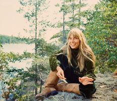 a woman sitting on top of a rock next to trees