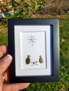 a person holding up a framed picture with two small rocks in the shape of a star