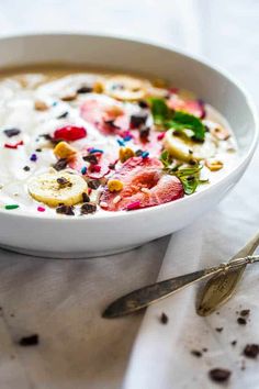 a white bowl filled with cereal and fruit on top of a table next to a spoon