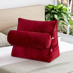 a red pillow sitting on top of a bed next to a plant