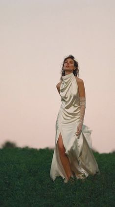 a woman in a white dress standing on top of a lush green field at sunset