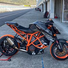 an orange and black motorcycle parked on the side of a road next to a building