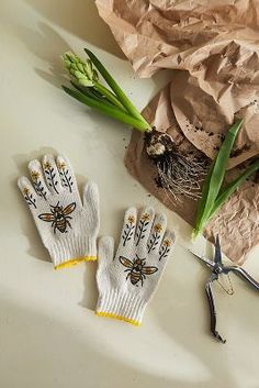 two gloves with flowers on them next to some scissors and paper bags that have plants growing out of them