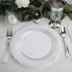 a white dinner plate with silverware on a marble table top next to greenery