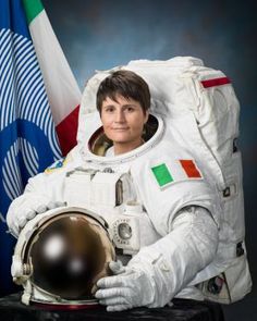 a woman in an astronaut's suit holding a helmet next to the flags of italy and italy