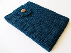 a blue crocheted bag with a button on the front is laying on a white surface