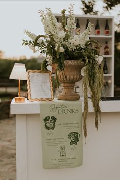 a vase with flowers sitting on top of a white counter next to a sign that says drinks