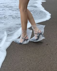 a woman's legs in clear plastic shoes on the beach