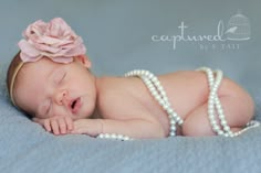 a baby is laying down wearing pearls and a pink flower on her head, with its eyes closed