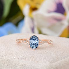 a blue and white diamond ring sitting on top of a cushioned surface with flowers in the background