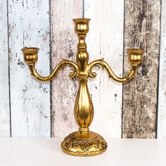 a gold candelabra with three candles on it against a white wooden wall