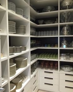 an organized pantry with white shelves and dishes on the bottom shelf, full of plates and bowls