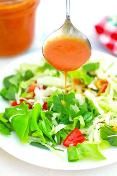 a salad with dressing being drizzled over it and sitting on a plate