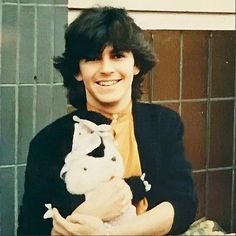 a young man holding a white dog in his arms and smiling at the camera while standing next to a tiled wall