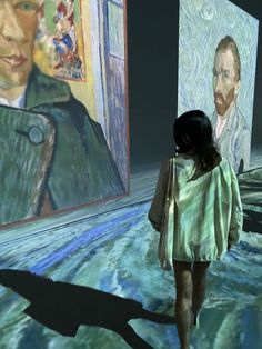 a woman is walking in front of two large paintings that are being projected on the wall