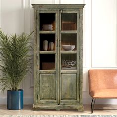 a green cabinet sitting next to a chair and potted plant in a living room