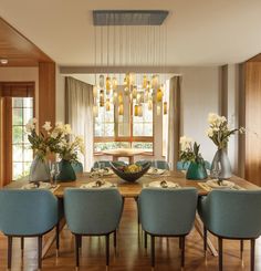 a dining room table with blue chairs and flowers in vases on the centerpiece