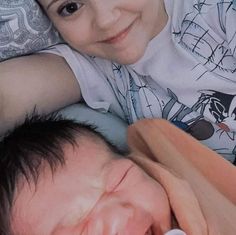 a young boy laying next to a baby on top of a bed