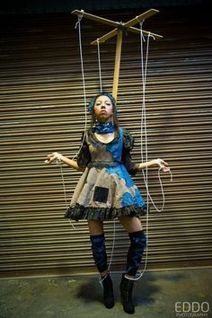 a woman dressed in costume is suspended by strings and wires with her hands up to the ceiling